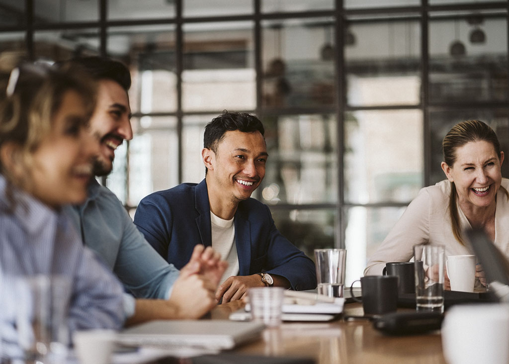 Smiling businessman looking away while sitting amidst cheerful colleagues at conference table